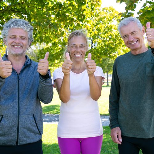 Cheerful sporty mature people standing together after morning exercises in park, looking at camera, smiling and showing thumbs up. Retirement or active lifestyle concept